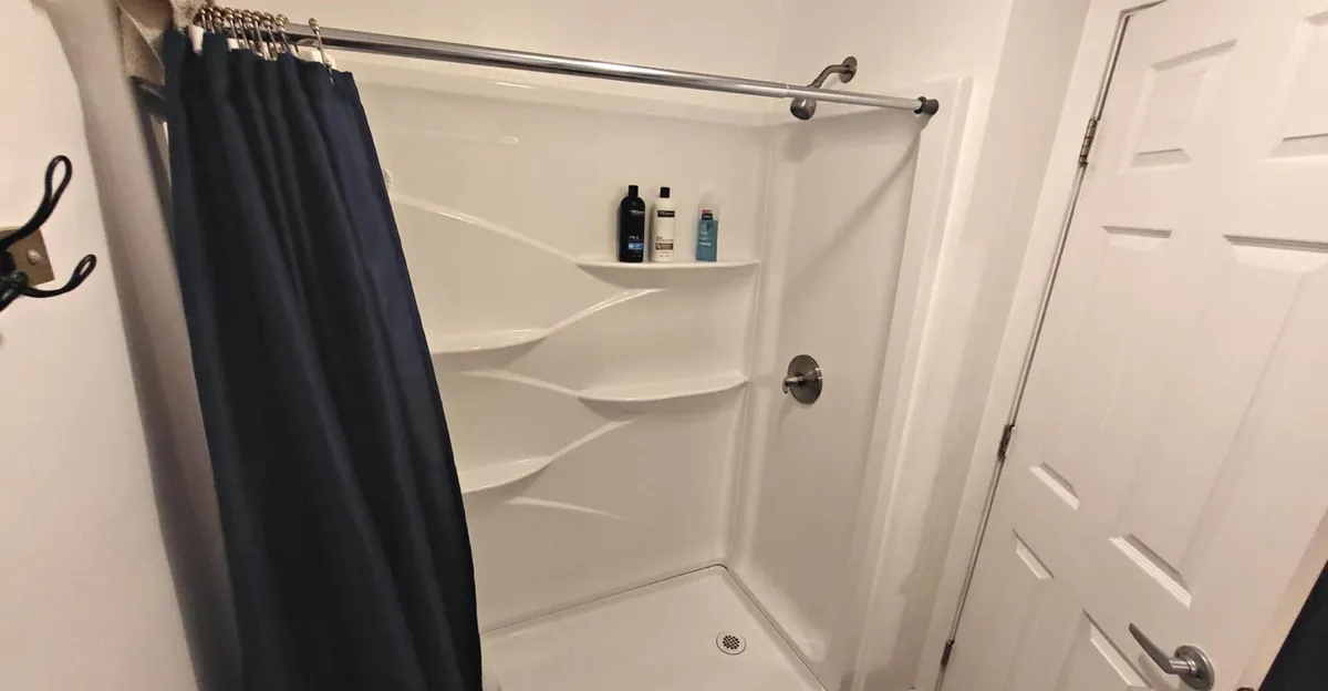 A close-up view of the shower area, highlighting a clean shower curtain and shelves lined with quality toiletries. The overall mood is calm and refreshing, evoking the sensation of an invigorating shower or tranquil bath within a private sanctuary.