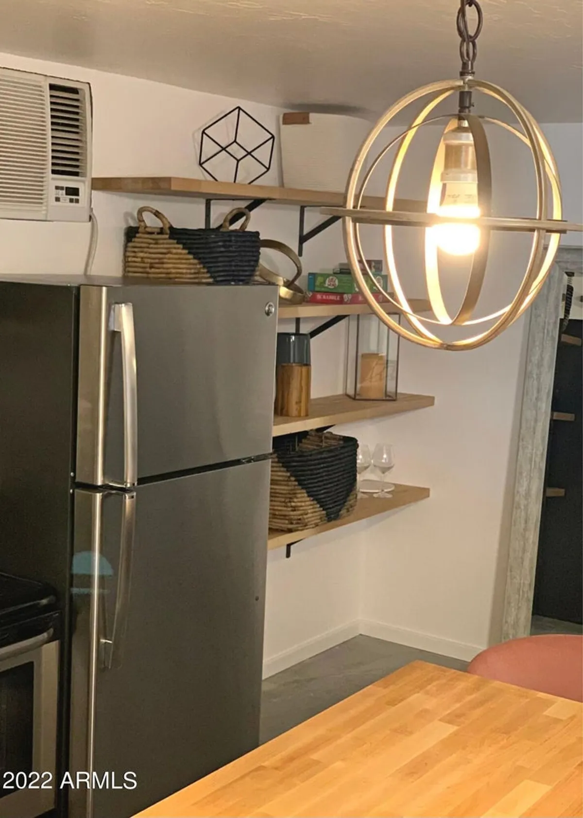 A modern kitchen scene featuring a striking light fixture, open shelving, and a gleaming stainless steel refrigerator. The setting is bright and contemporary, designed for both cooking and casual entertaining.