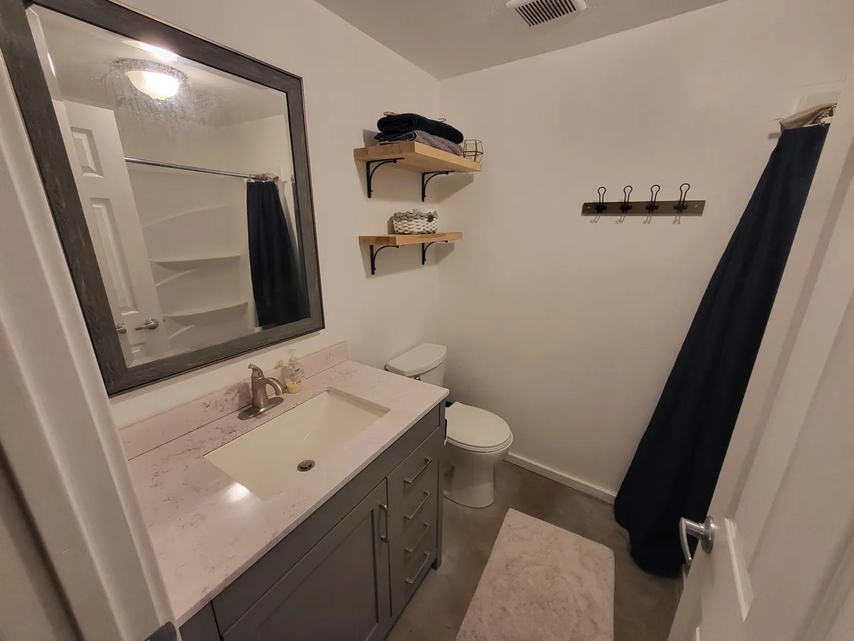 A second angle of the bathroom space, displaying the vanity and mirror against organized shelves. The arrangement is minimalist and tidy, with an emphasis on personal grooming and solitude, reinforcing the bathroom’s role as a private sanctuary.