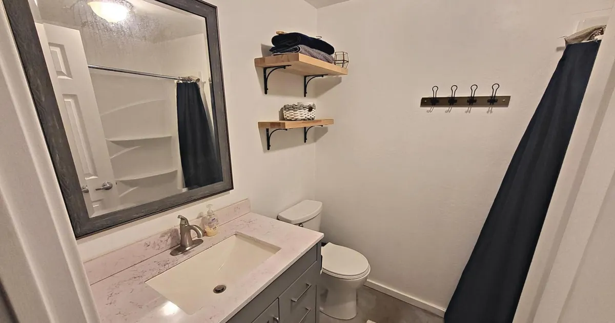 This image features a bathroom vanity with a sleek sink and a large mirror, complemented by shelves neatly stacked with crisp towels and a visible shower curtain in the background. The tidy arrangement and modern fixtures create an inviting, spa-like atmosphere ideal for relaxation and self-care.