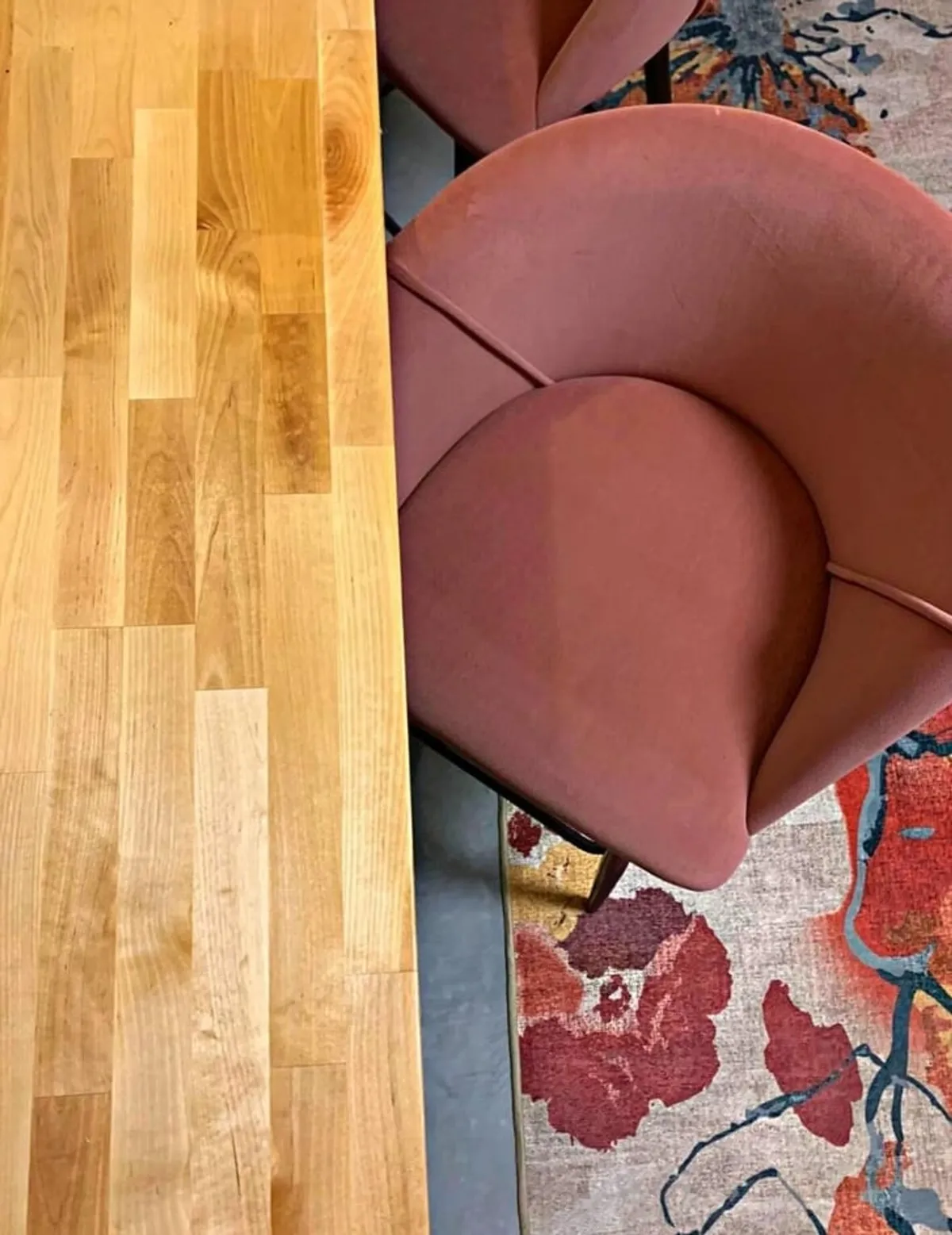 A cozy dining nook featuring a wooden table surface, a plush pink upholstered chair, and a vibrant area rug beneath. The intimate setting is perfect for coffee conversations or romantic dinners.