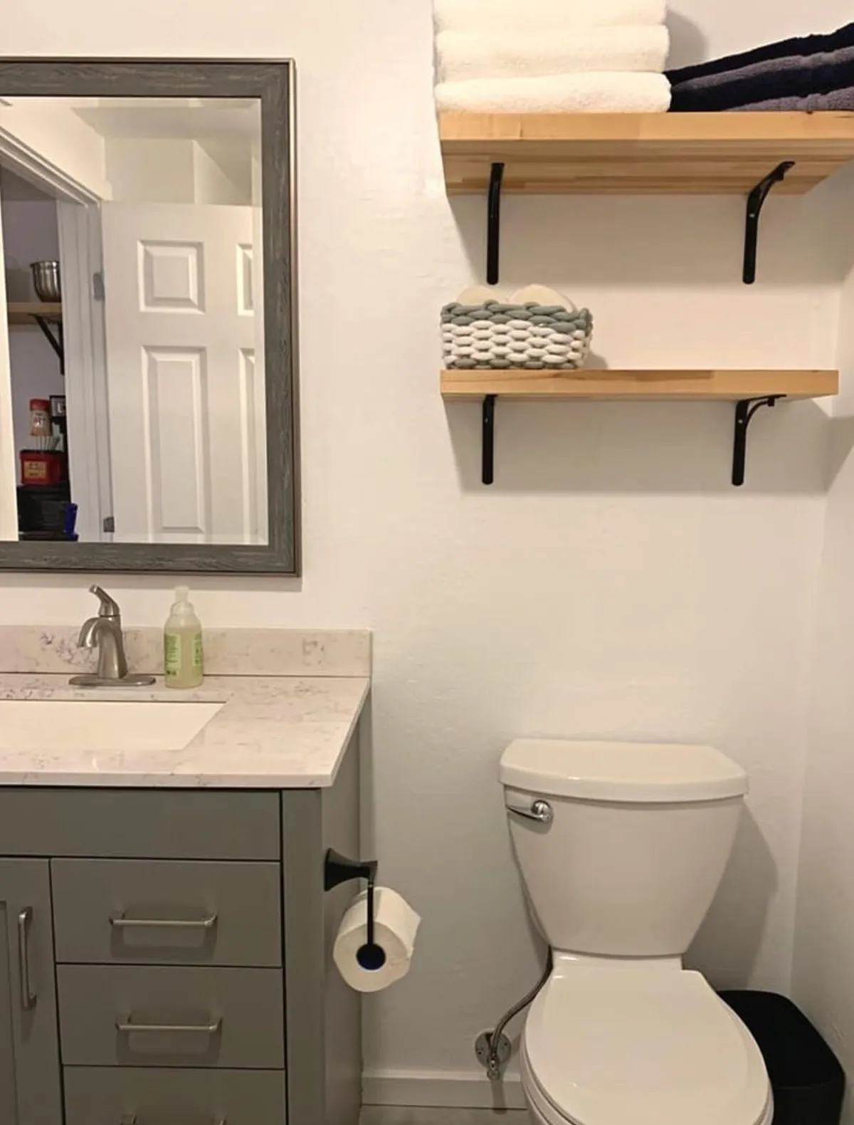 An inviting bathroom scene showcasing a mirror, sink, toilet, shelves with neatly arranged towels, and soft accent lighting. The space feels functional yet welcoming, perfect for personal grooming rituals that bookend a restful night.